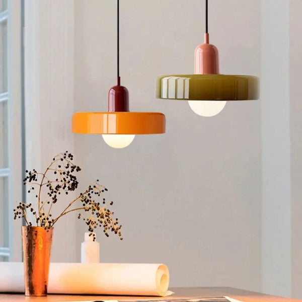 Deux lampes plafonniers design rétro colorées, l’une orange et l’autre vert olive, suspendues au-dessus d’une table moderne, diffusant une lumière douce et chaleureuse.