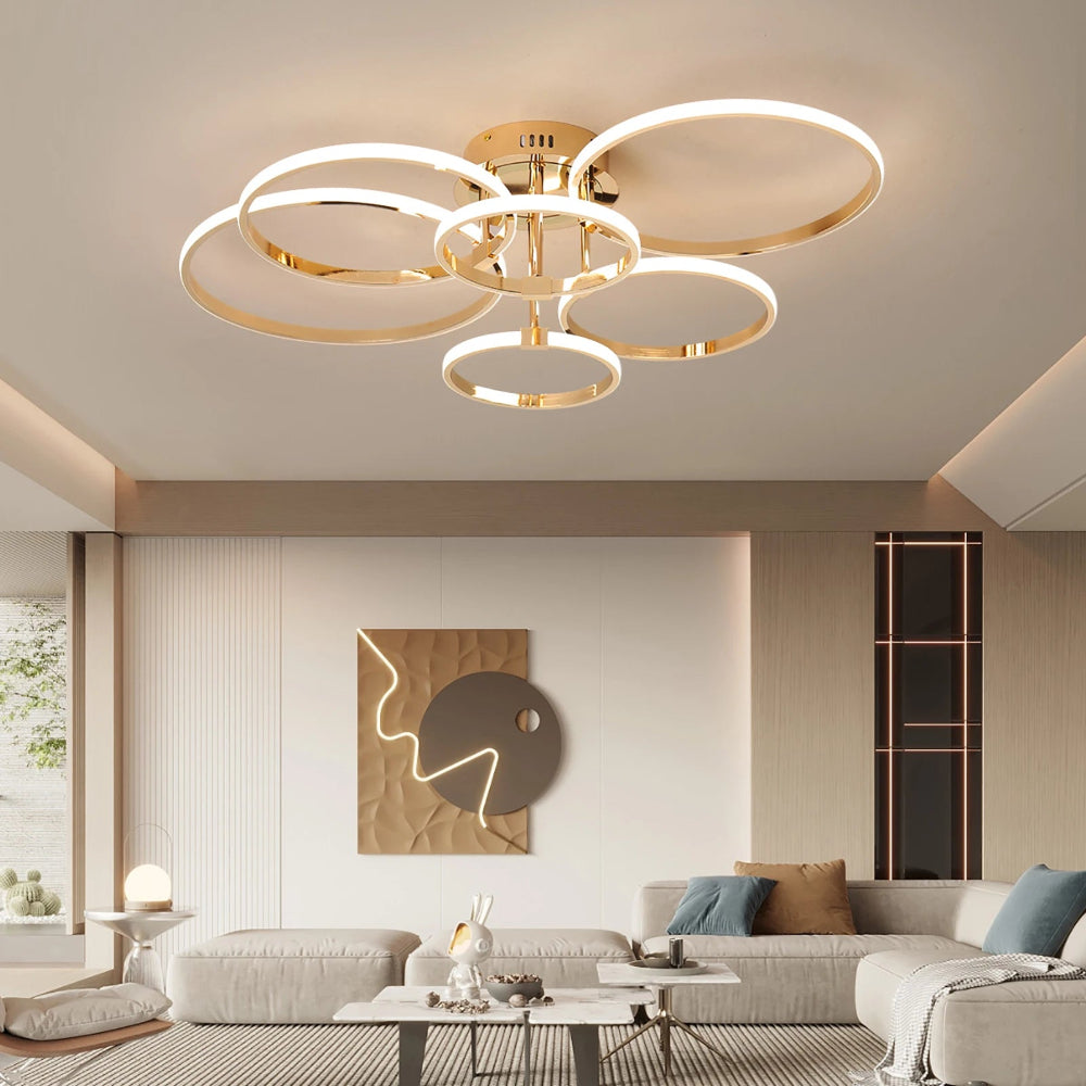 Plafonnier moderne à anneaux LED entrelacés en finition dorée, diffusant une lumière douce et homogène dans un salon contemporain élégant.