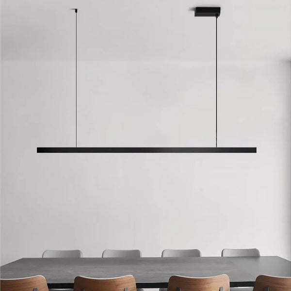 Plafonnier nordique minimaliste suspendu, en forme de barre fine noire, installé au-dessus d’une table de salle à manger moderne.